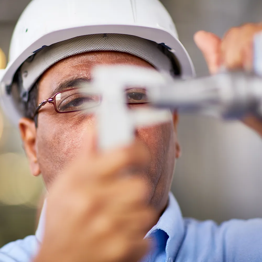 man with hard hat measuring item with caliper